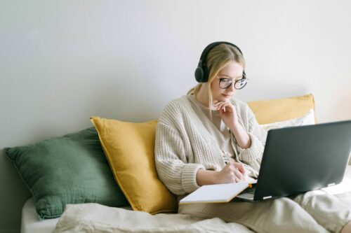 woman with headphones taking notes from her laptop