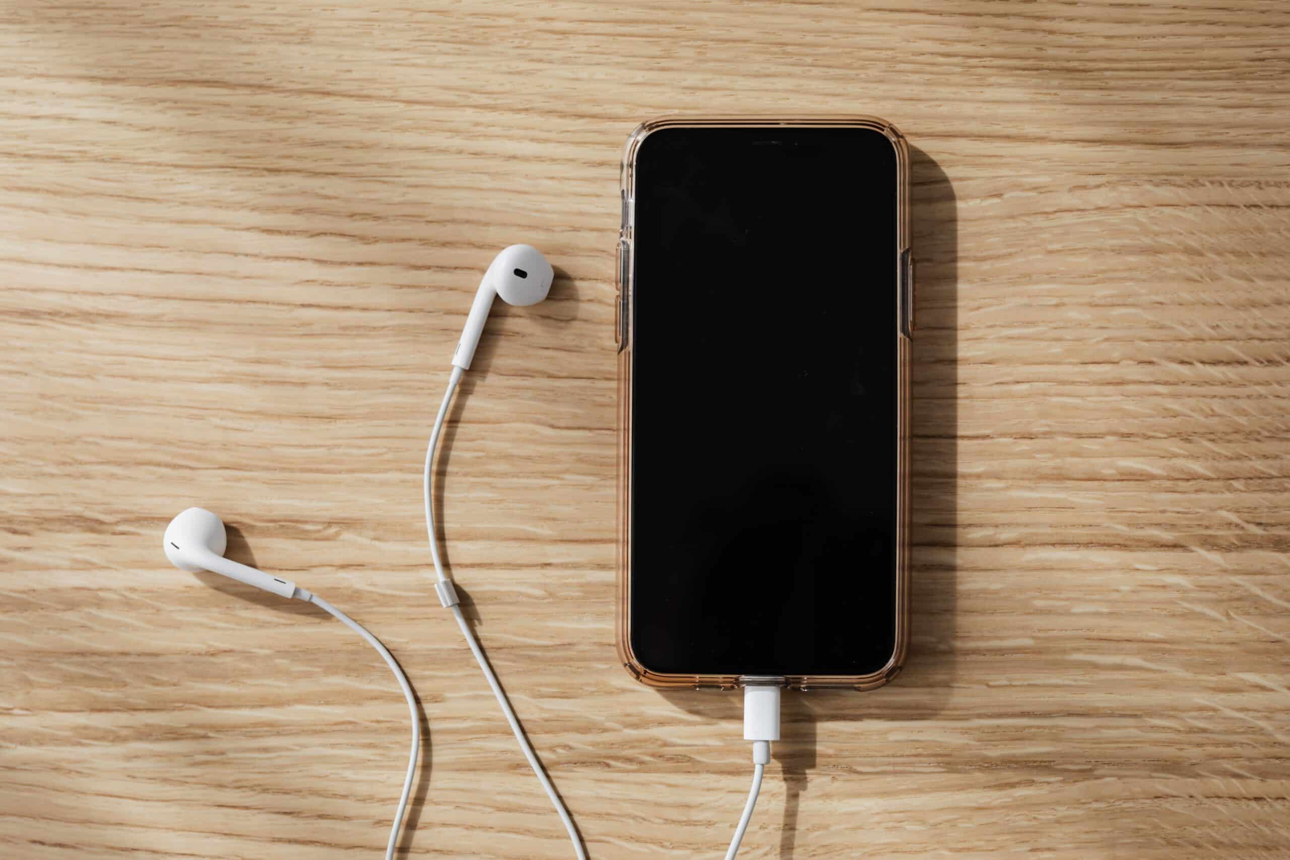 charging smart phone with white earbuds on a wooden table